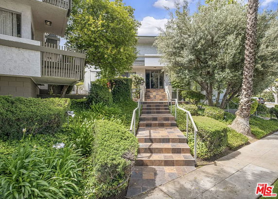 Front view of a multi-story residential building with a tiled staircase and lush greenery.