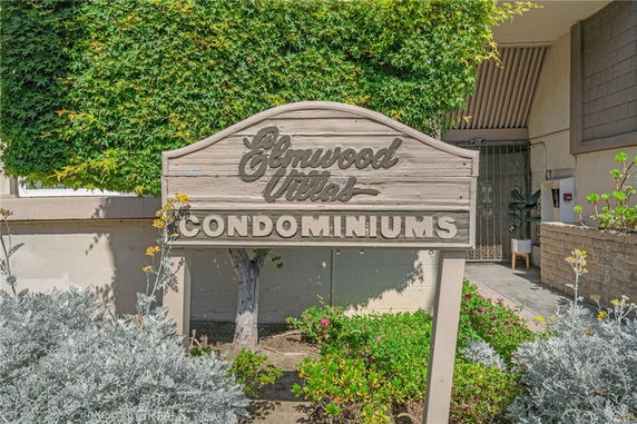 Front view of a condominium building with a wooden sign reading 'Condominiums' and surrounding greenery.