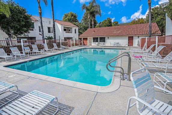 Outdoor swimming pool area with white lounge chairs and surrounding buildings.