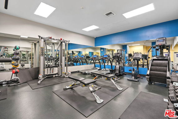 Indoor gym area with various exercise equipment including treadmills, weight machines, and dumbbells.