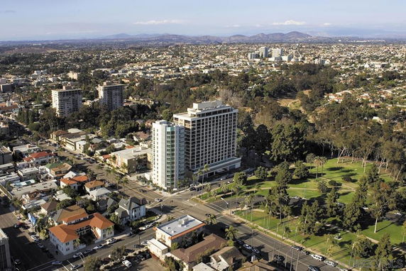 Aerial view of a cityscape featuring high-rise buildings, residential areas, and a nearby park.