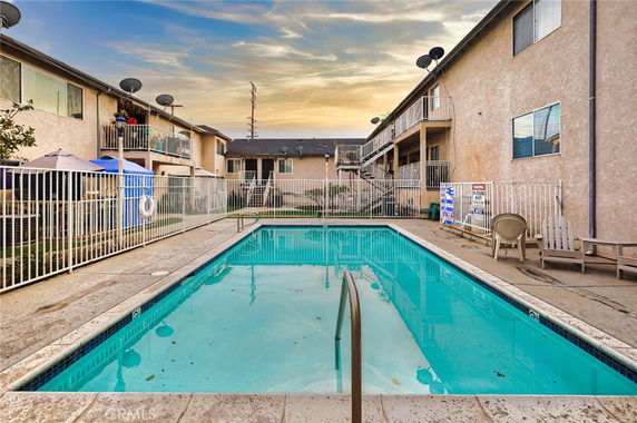 Outdoor swimming pool surrounded by a fence with two-story residential buildings in the background.