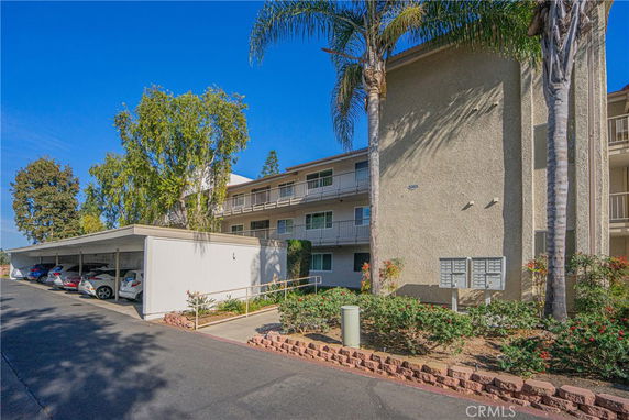 Front view of a multi-story residential building with balconies and covered parking area.