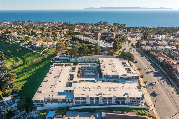 Aerial panoramic view of a coastal residential area with houses, green spaces, and a clear ocean view in the distance.