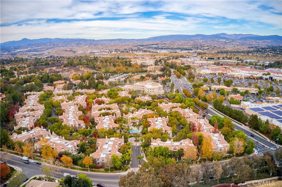 Aerial panoramic view of a residential area with rows of houses surrounded by trees and distant mountains.