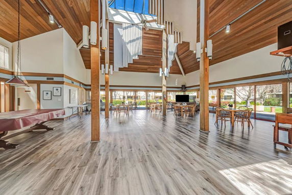 Interior view of a clubhouse with wooden flooring, high ceilings, tables, chairs, and large windows.