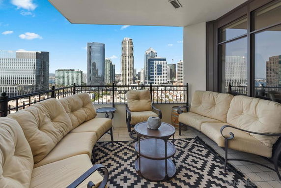 Balcony view with outdoor seating, overlooking a cityscape with tall buildings.