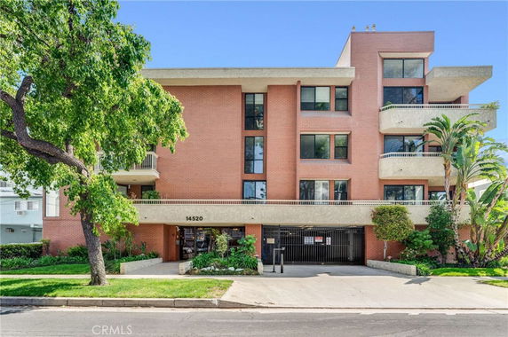 Front view of a multi-story apartment building with balconies and a gated entrance.
