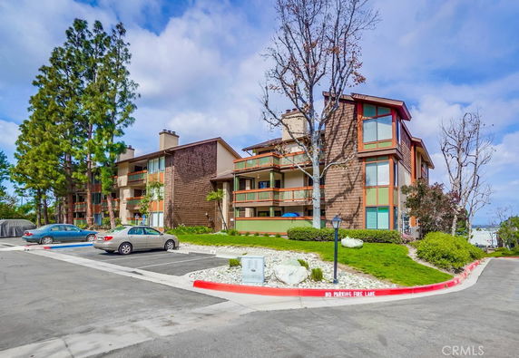 Front view of a multi-story apartment building with balconies and parking area in foreground.