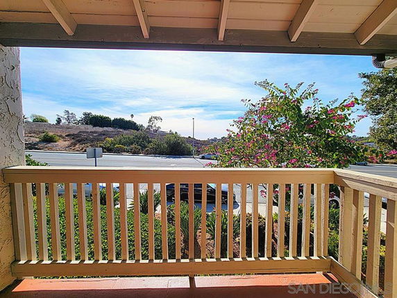 View from a balcony overlooking a road, with trees and hills in the distance.