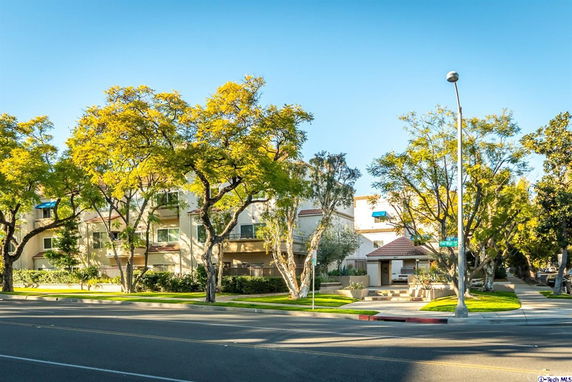 Front view of a multi-story residential building with balconies and surrounding trees.