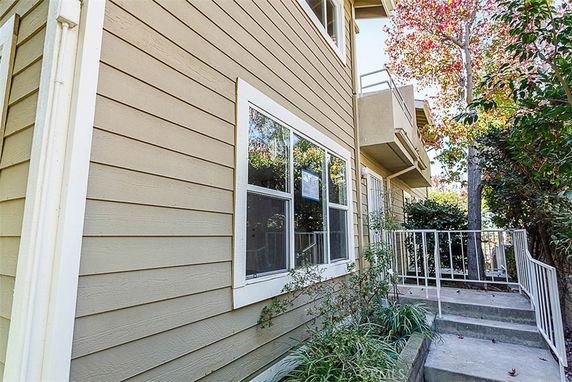 Exterior view of a multi-story house with beige siding and white-trimmed windows, featuring a balcony and a small patio entrance.