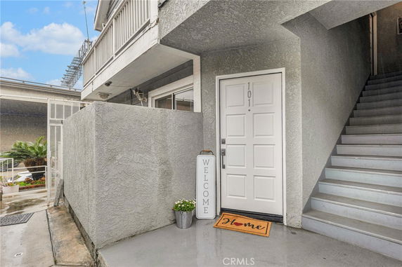 Front view of a building entrance with stairs leading up and a welcome sign by the door.