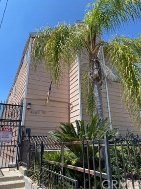 Front view of a multi-story building with a palm tree and metal fence.