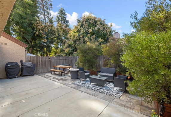 Outdoor patio area with seating, table, and grill surrounded by trees and wooden fence.