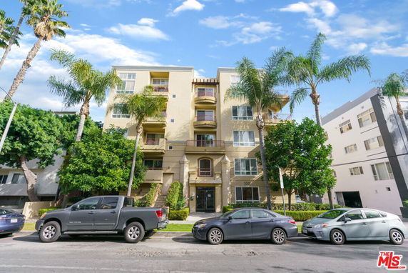 Front view of a multi-story residential building with balconies and palm trees.