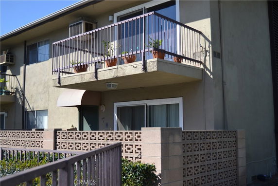 Front view of a two-story apartment building with balconies and potted plants.