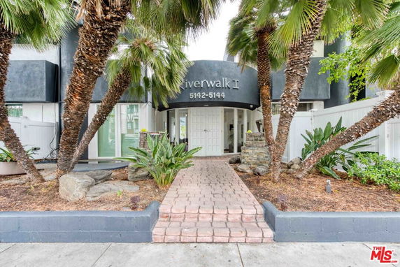 Front entrance of a residential building with a pathway and palm trees.