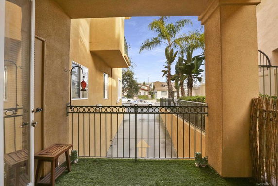 Outdoor view from a gated patio area of a building, showing neighboring buildings and palm trees.