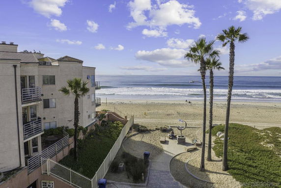 Panoramic view of a beachfront beside a building with palm trees, sandy beach, and ocean waves.