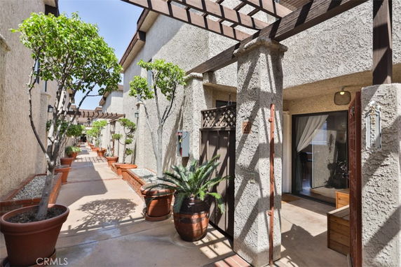 Outdoor view of a residential building with multiple units, featuring potted plants and a wooden pergola.