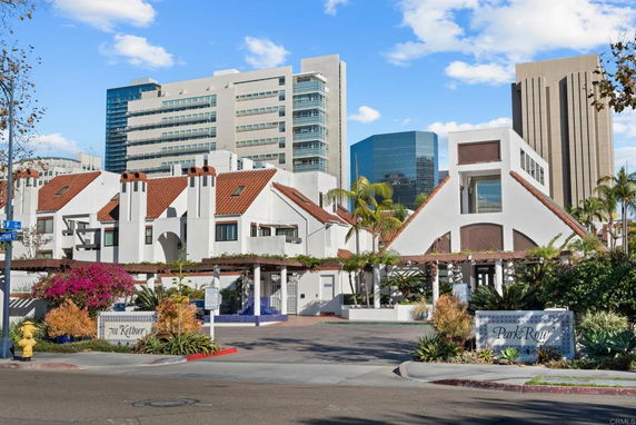 Front view of a complex with red-tiled roofs and white walls, situated in an urban area with high-rise buildings in the background.