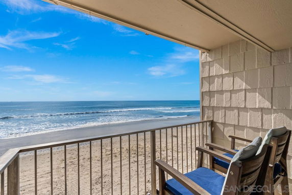Balcony overlooking a sandy beach and ocean under a blue sky.