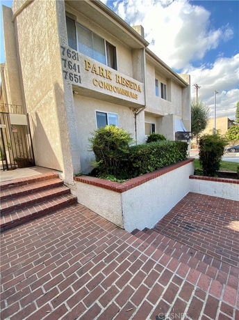 Front view of a condominium building with a brick pathway and external staircase.