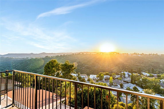 Panoramic view from a balcony overlooking a valley and distant hills with the sun setting on the horizon.