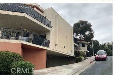 Side view of a modern multi-level building with a sloped driveway and balconies.
