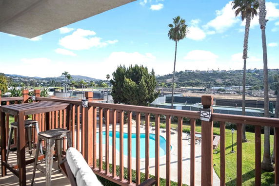 View from balcony overlooking a swimming pool and tennis courts with hills in the background.