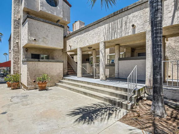 Front view of a multi-story building with stucco walls and a staircase leading to the entrance.