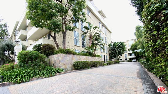 Front view of a multi-story residential building with balconies, surrounded by trees and greenery.