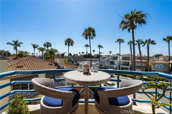 Panoramic view from a balcony overlooking rooftops and palm trees under a clear blue sky.