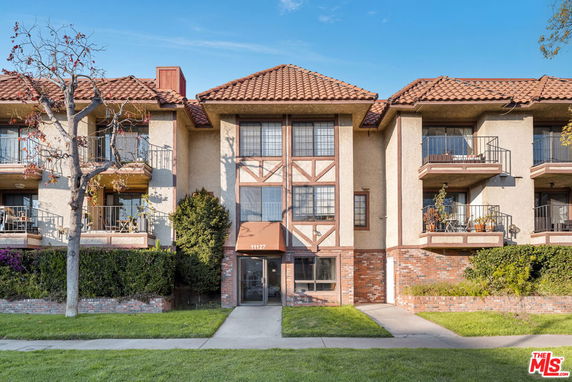 Front view of a multi-story residential building with balconies and a tiled roof.
