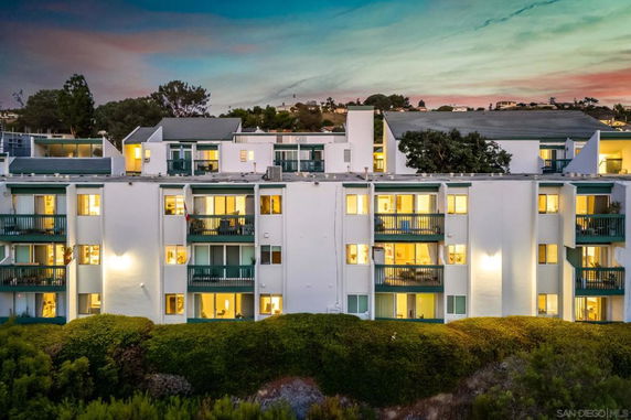 Front view of a multi-story building with balconies and illuminated windows at dusk.