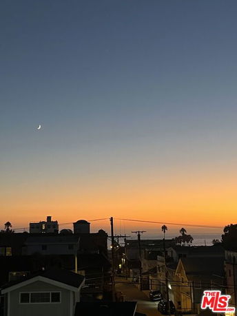 Panoramic view of a sunset over a coastal area with buildings and a crescent moon in the sky.