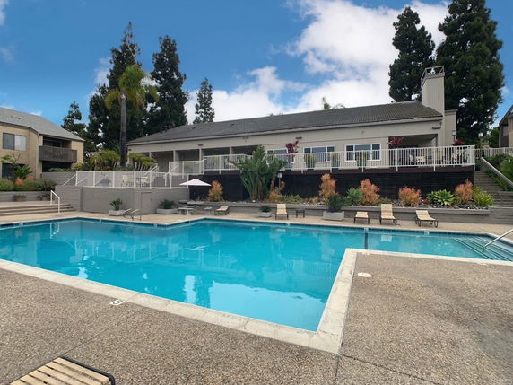 Outdoor swimming pool with lounge chairs and a residential building in the background.
