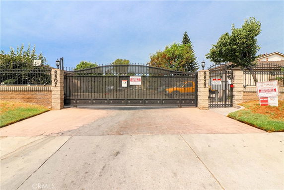 Front view of gated entrance to a property with brick pillars and iron fence.