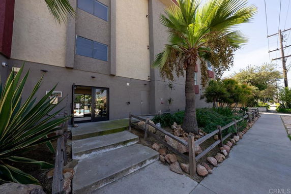 Front view of a multi-story building with a glass entrance and surrounding landscaping.