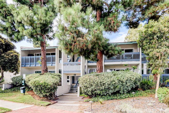 Front view of a two-story building with balconies and surrounding trees.
