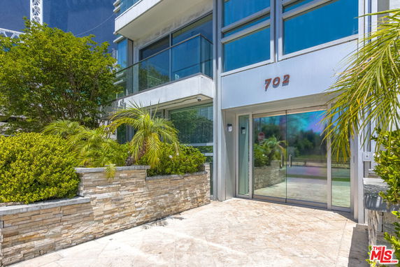 Front view of a modern building entrance with large glass doors and the number '702' above.