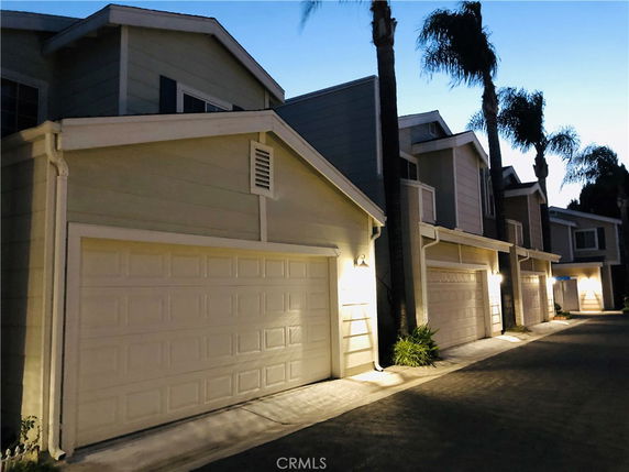 Front view of garage doors in a row of connected townhouses at dusk.