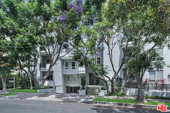 Front view of a multi-story building with balconies and surrounding trees.