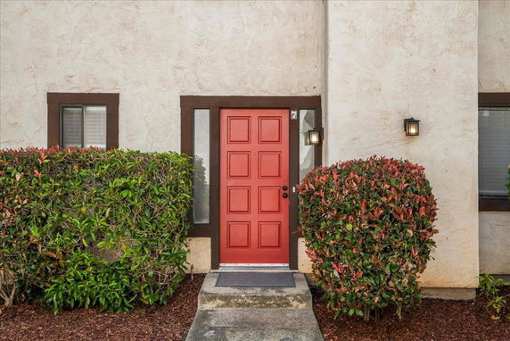 Front view of a house with a red door and two windows, surrounded by shrubs.