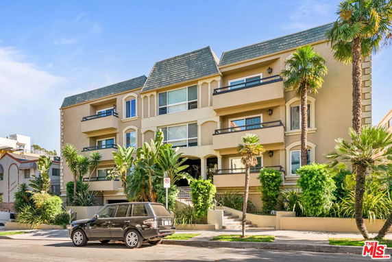 Front view of a multi-story residential building with balconies and palm trees.