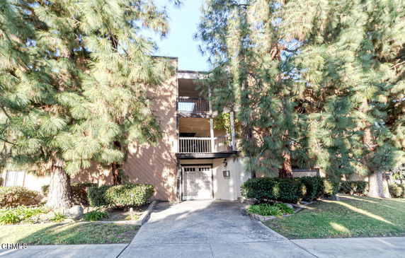 Front view of a multi-story residential building with balconies and surrounded by trees.