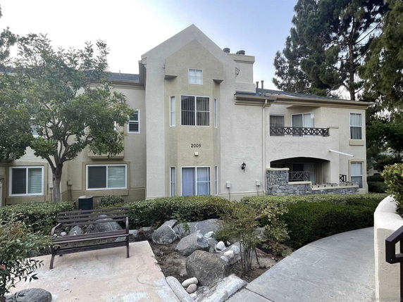 Front view of a two-story residential building with balconies and a bench in the garden.