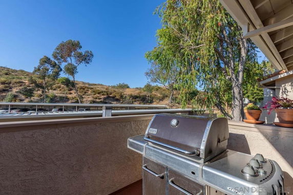 Outdoor patio with a barbecue grill, overlooking a hillside with trees.