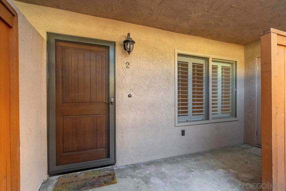 Front view of a house entrance with a brown wooden door and a window with shutters.